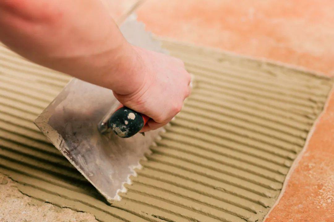 在施工基面上将瓷砖粘合剂梳刮成条纹状,然后按顺序将瓷砖粘贴在胶泥