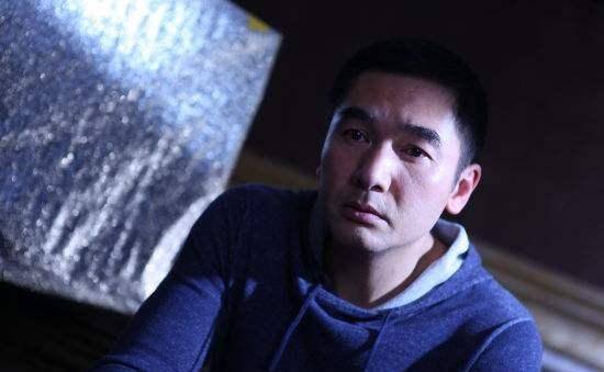 照片中的方中信身穿灰色短袖体恤衫配黑色的运动裤,站在山顶上对着