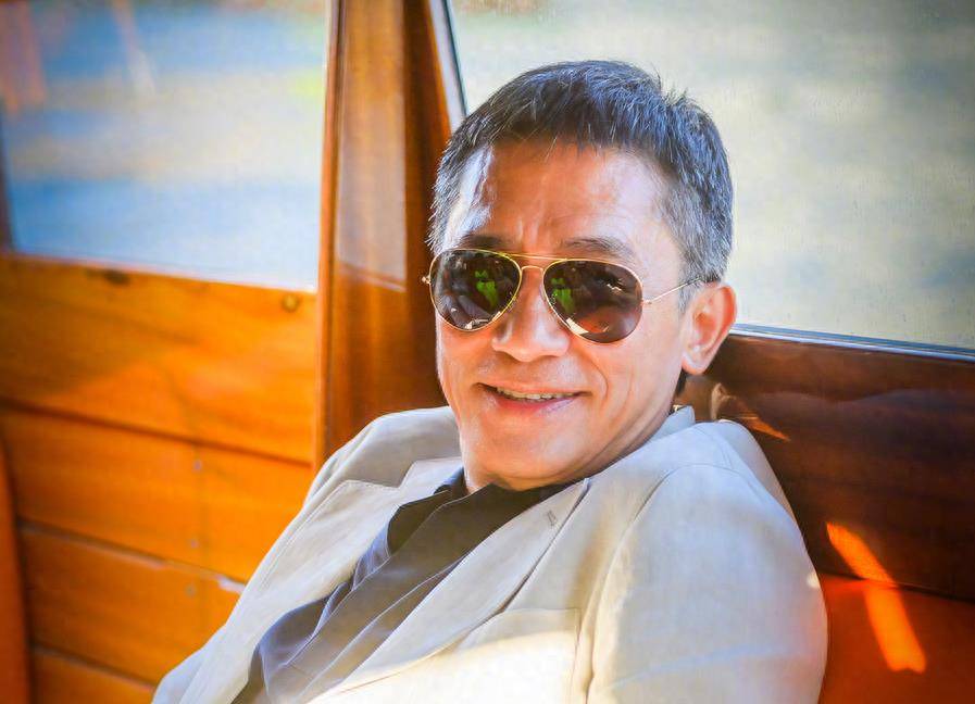 梁朝伟穿着白色t恤,戴着墨镜,靠在船甲板上.