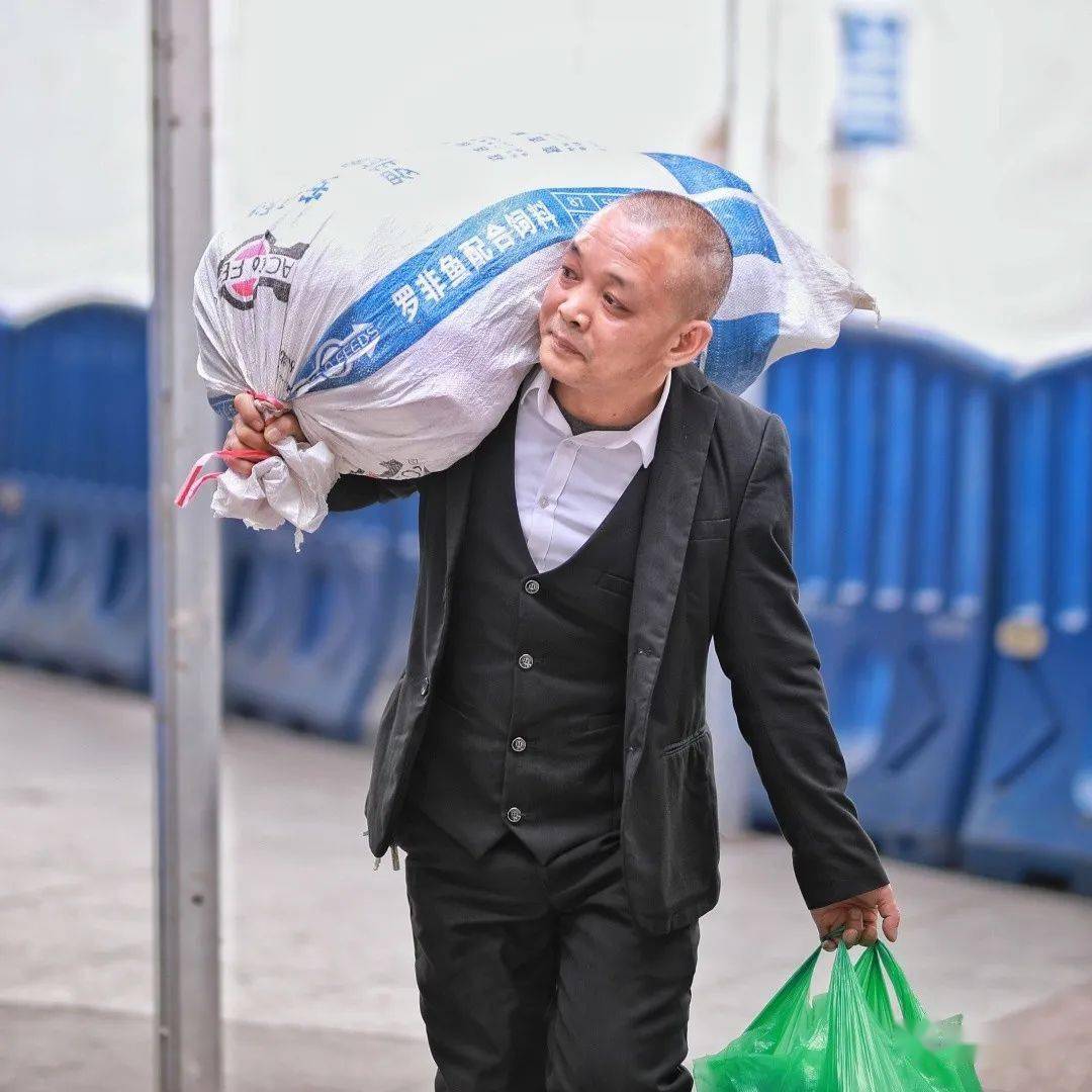 日,佛山火车站前广场,一位穿着礼服的男士扛着蛇皮袋装的行李进站返乡