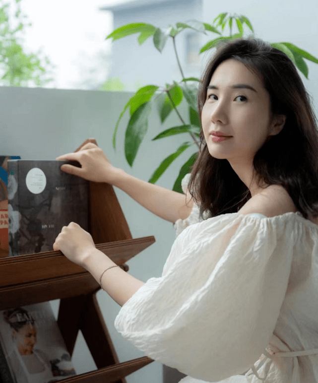 董花花长发披肩,化着淡妆,身穿一字肩白裙出镜,蹲