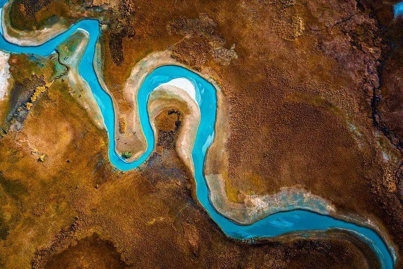 在无人机俯瞰视角拍摄下,蔚蓝的河流呈现出简约的线条形式,与褐色的
