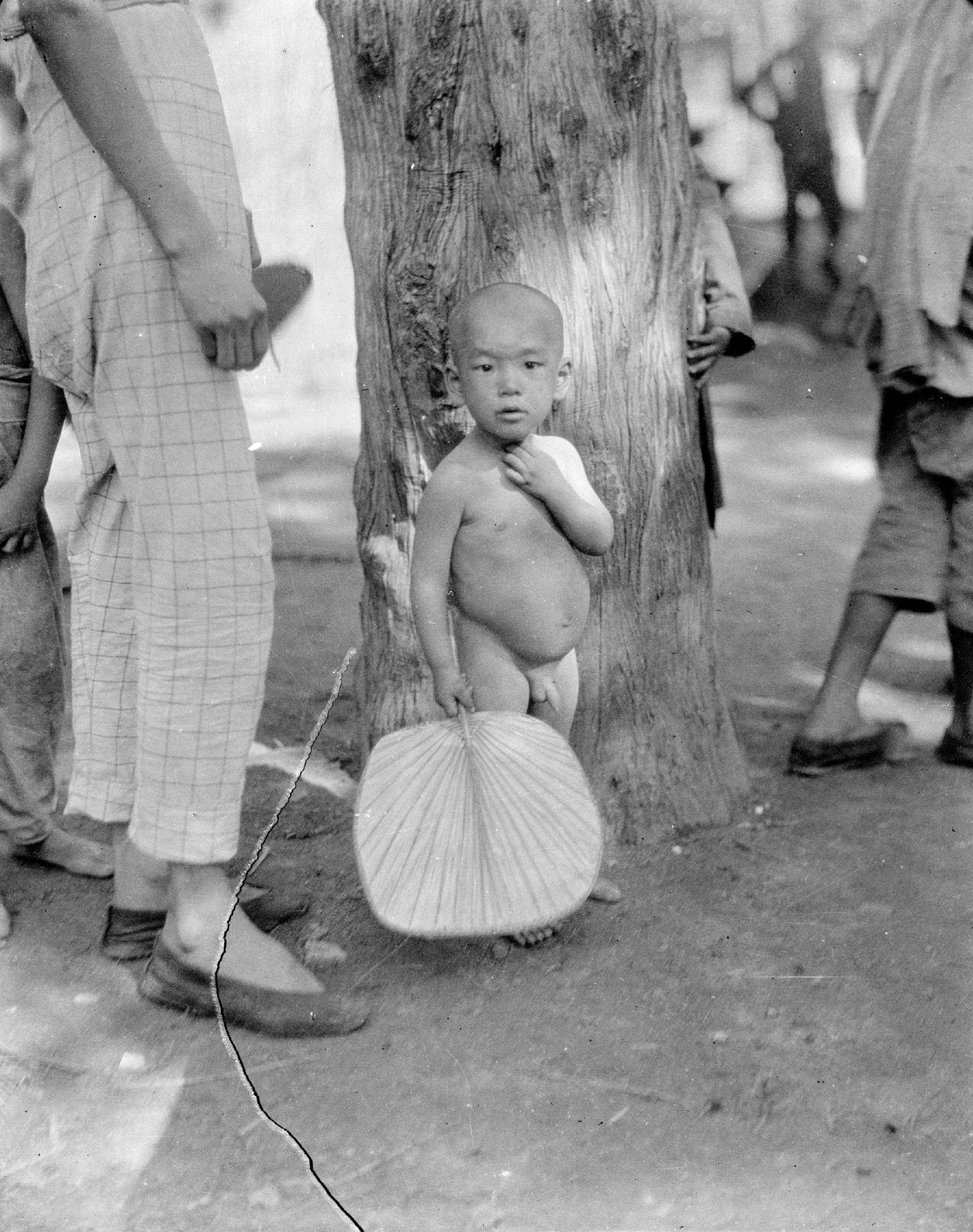 15,在宜昌街头,一位小男孩可能是怕热,光着身子,手里拿着芭蕉扇,站在